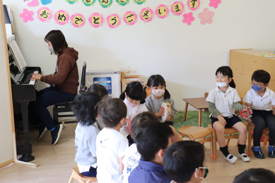 椅子に座って歌っている園児とピアノを弾いている先生